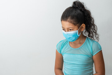 little girl (8 years old) sitting with her arms down confused brown girl receiving a news with a blue surgical mask. Medical, pharmaceutical and sanitary concept.