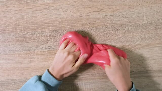 Playing with slime, stretching the gooey substance for fun and stress relief. Close up and top view of female hand holding red shining slime and squeezing it. 4K resolution video.