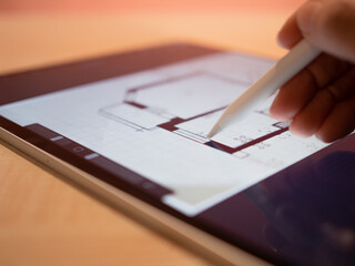 architectural engineer is working on a floor plan of building on mobile tablet computer. architect's hand draws with stylus on screen, plan of apartment, close-up. Mobile gadgets for professional work