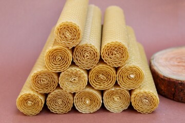 Hand rolled beeswax candle on dark rose background 