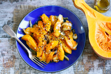 Pieces of baked pumpkin with onions on a blue plate. Pumpkin recipe. Autumn food. Vegan diet.