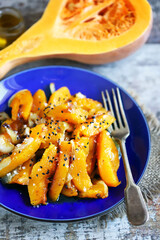 Pieces of baked pumpkin with onions on a blue plate. Pumpkin recipe. Autumn food. Vegan diet.