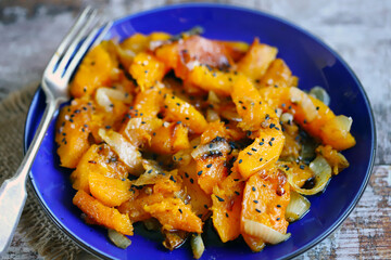 Pieces of baked pumpkin with onions on a blue plate. Pumpkin recipe. Autumn food. Vegan diet.