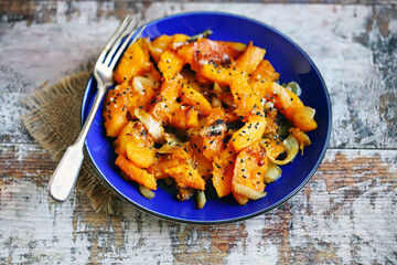 Pieces of baked pumpkin with onions on a blue plate. Pumpkin recipe. Autumn food. Vegan diet.