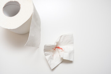 Used sheet of bloody toilet paper and a roll on white background, hemorrhoids and rectal bleeding concept - obrazy, fototapety, plakaty