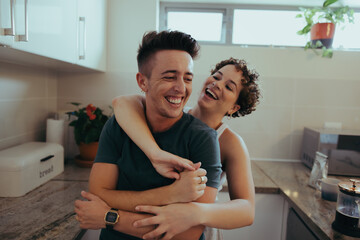Romantic queer couple laughing together in their kitchen - obrazy, fototapety, plakaty
