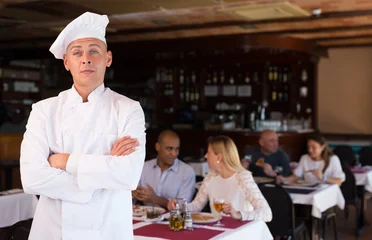  Portrait of confident professional pizzeria chef in restaurant hall on background with guests © JackF