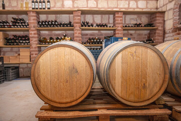 Closeup red wine glass on background of wooden oak barrels stacked in straight rows in order in cellar of wine, vault. Concept professional degustation, winelover, sommelier travel.