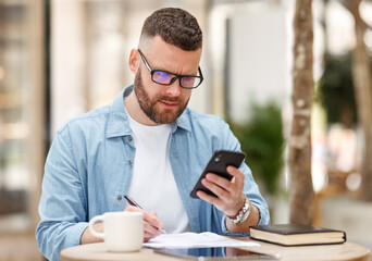 Young man in eyeglasses watching educational video on mobile phone, studying online at outdoor cafe