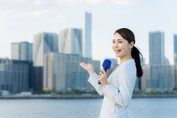 都市の前に立つ女性アナウンサー