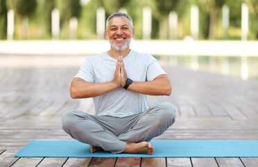 Calm happy mature man sitting in lotus pose on mat during morning meditation in park