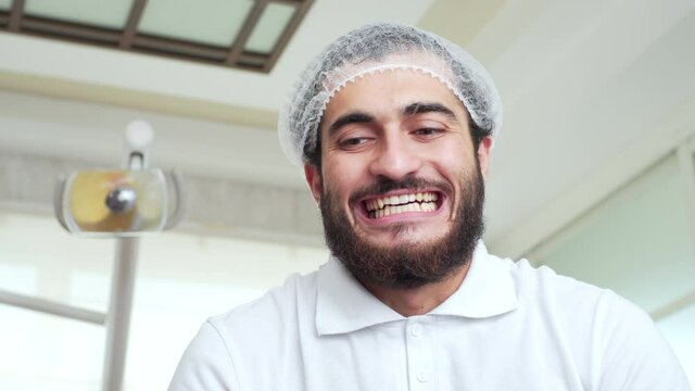 A bearded dentist is showing a patient how to show their theeth and raising hands with diagnostic instruments. POV. Funny doctor. Oral hygiene and dental cure in dentistry