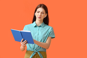 Displeased young woman with earphones and book on color background