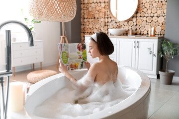 Young woman reading magazine while taking bath at home
