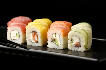 Plate with delicious sushi rolls on dark background