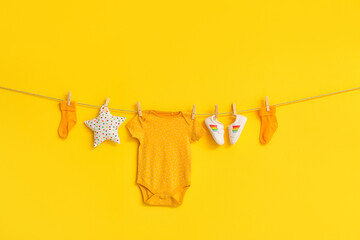Stylish baby clothes, shoes and toy hanging on rope against color background