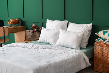 Bed with soft pillows and blanket near green wall