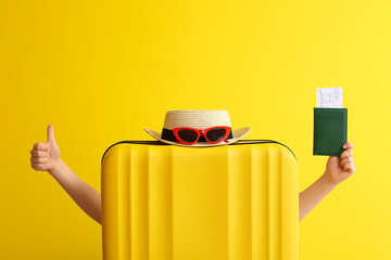 Young woman with suitcase and passport showing thumb-up on color background