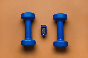 Pulse oximeter and dumbbells on color background