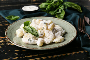 Plate of tasty gnocchi with creamy sauce on black wooden background