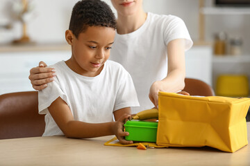 Mother and her little son putting lunch in bag before school