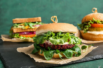 Board with tasty vegetarian burgers on green background