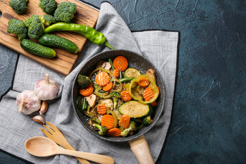 Frying pan with different vegetables on dark background