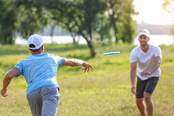 Young men playing frisbee in park - obrazy, fototapety, plakaty