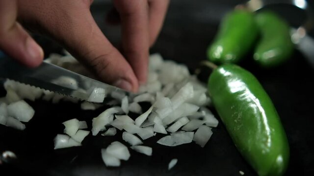 Hands chopping onion and green chili peppers on a traditional Mexican comal