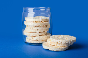 Glass jar with puffed rice crackers on blue background