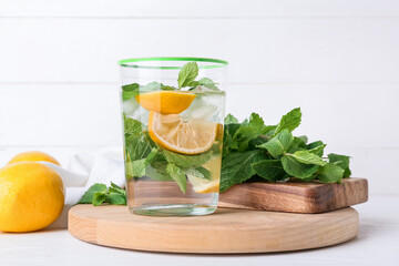 Glass of tasty mint tea with lemon on white wooden background
