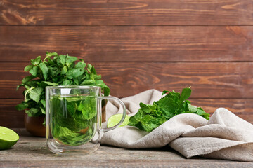Glass cup of tasty mint tea on wooden background
