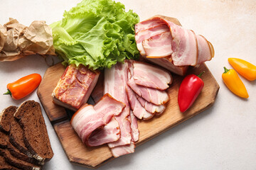 Wooden board with tasty smoked bacon, bread and fresh vegetables on light background