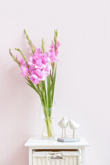 Vase with beautiful gladiolus flowers on table against color wall