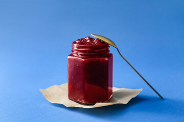 Jar of tasty cranberry jam on blue background