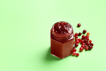 Jar with tasty cranberry jam and berries on green background