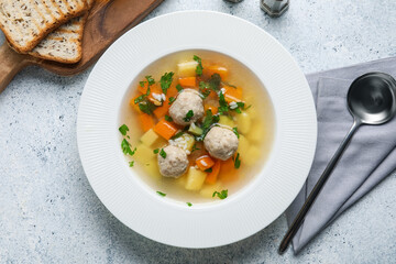 Bowl with tasty meatball soup and bread on light table
