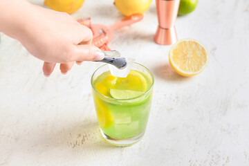 Woman putting ice cube in glass with tasty lemonade on light background