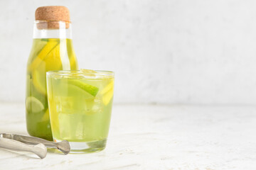 Glass and bottle with tasty lemonade on light background