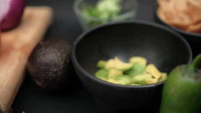 Chili peppers and bowls of chopped avocado and refried beans on black surface