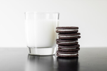 A classic picture of a stack of chocolate sandwich cookies next to glass of milk - obrazy, fototapety, plakaty