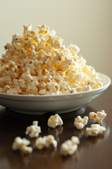 Overflowing white bowl of buttery popcorn on a dark table against a light beige wall