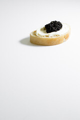 An isolated piece of toast topped with mascarpone cheese and black caviar on white surface
