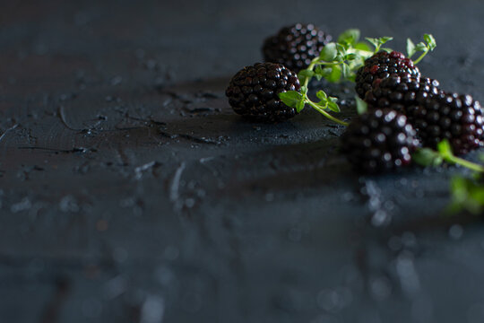 Plump blackberries and fresh thyme scattered on a rough, dark surface.