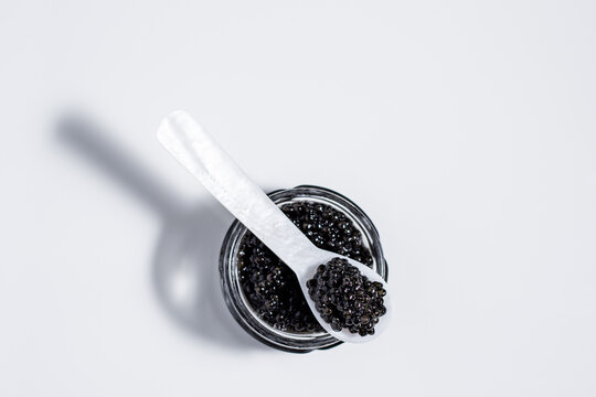 A mother-of-pearl spoon of black caviar resting on small jar