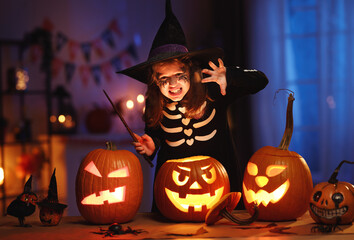 Little girl in witch hat and skeleton costume with magic wand in hand with frightening face