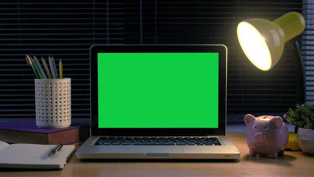 Chroma key green screen laptop computer set up for work on home office at night.	
