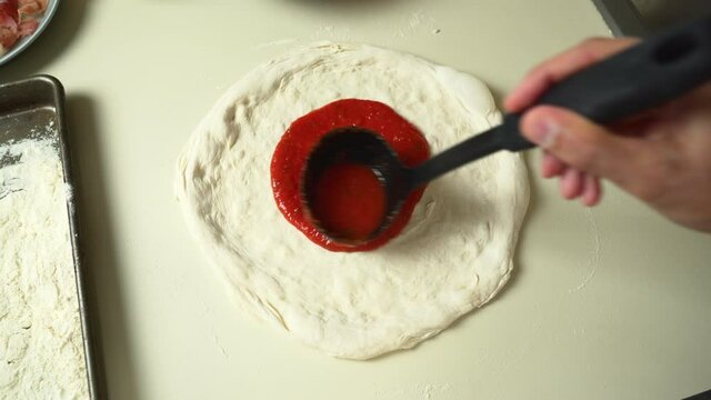 Top view of Chef while spreading Tomato Sauce on Pizza Dough with a Ladle in Traditional Italian Pizza's Restaurant. Italian Food. Pizza's Making.