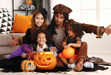 African american family in Halloween costumes making scary gesture while sitting with jack o lantern