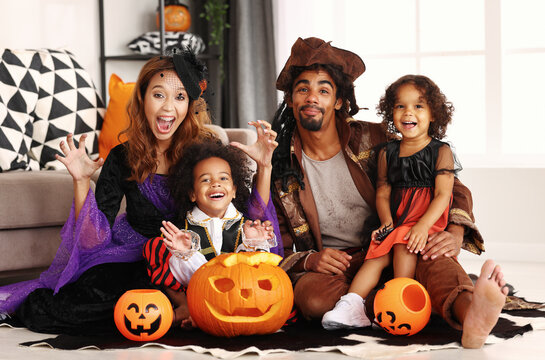 African american family in Halloween costumes making scary gesture while sitting with jack o lantern - Powered by Adobe